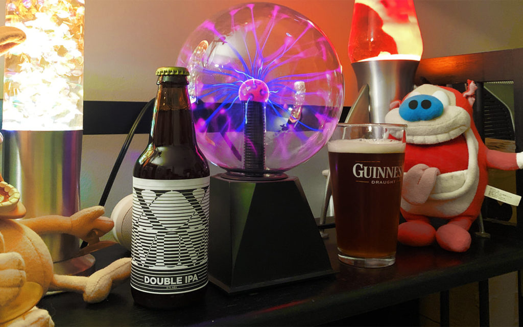 A bottle of MMXX double IPA on a shelf with a glowing tesla ball and Stimpy plush doll